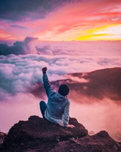 A man Seat in hill and rising his left hand to the sky for his success